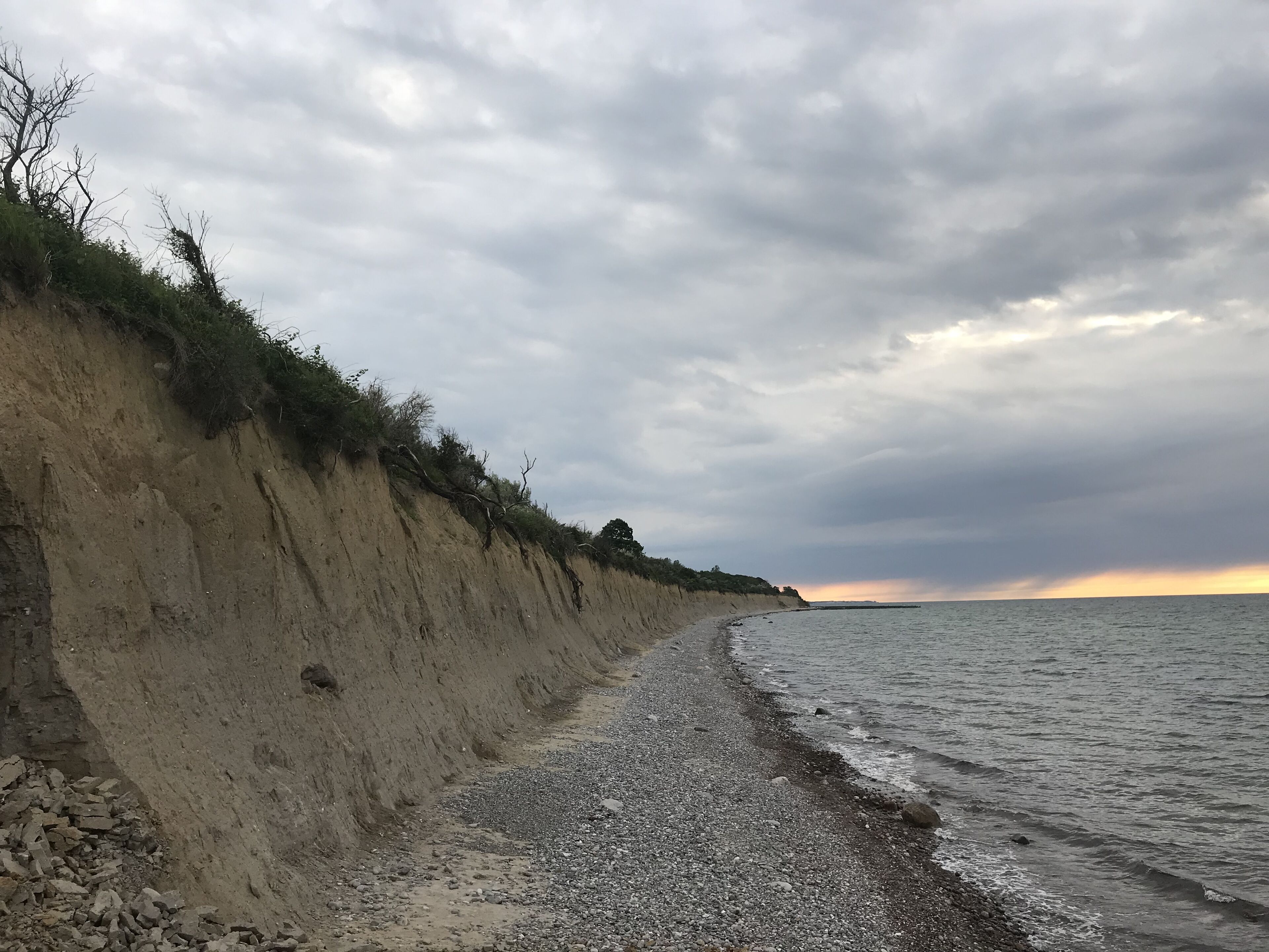 Paisagem costeira com uma praia arenosa, um penhasco íngreme e céu nublado.