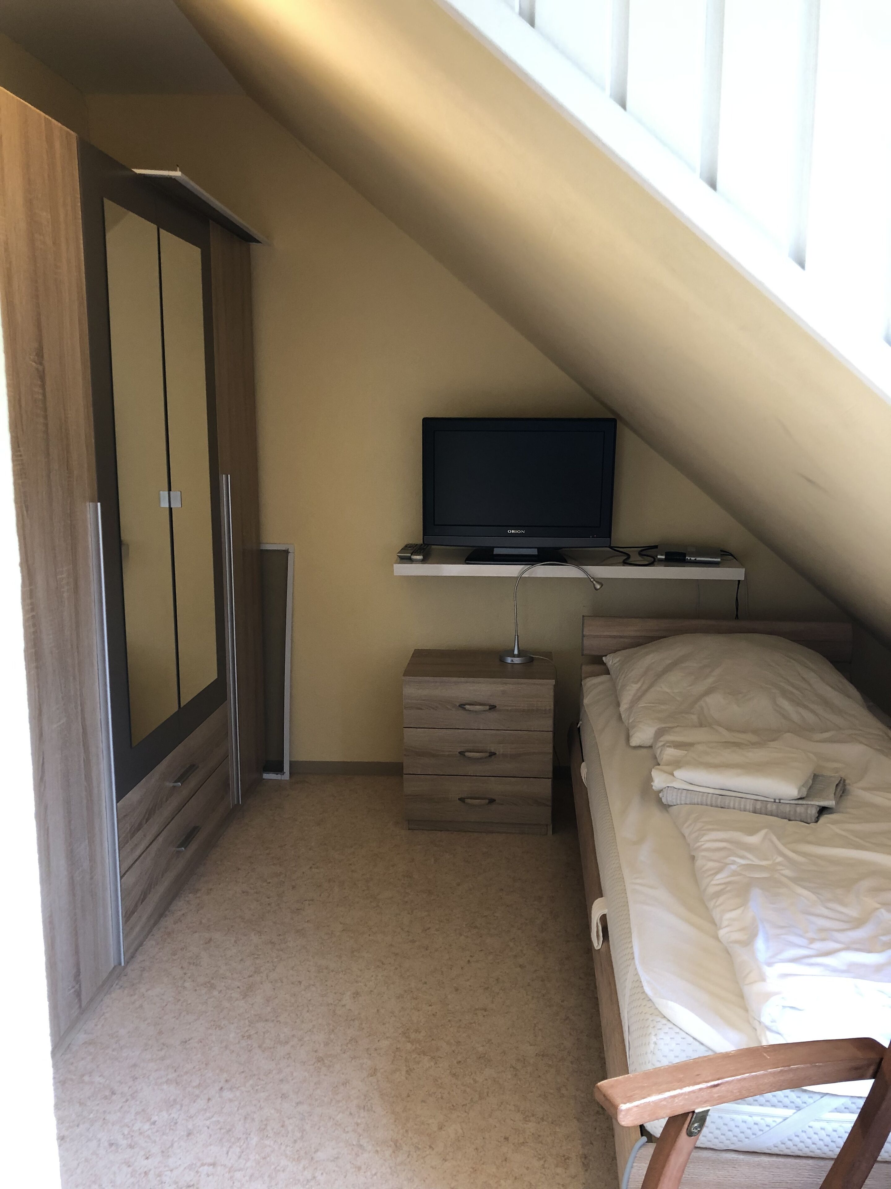 Un dormitorio con cama, televisor en un estante, armario y escritorio.