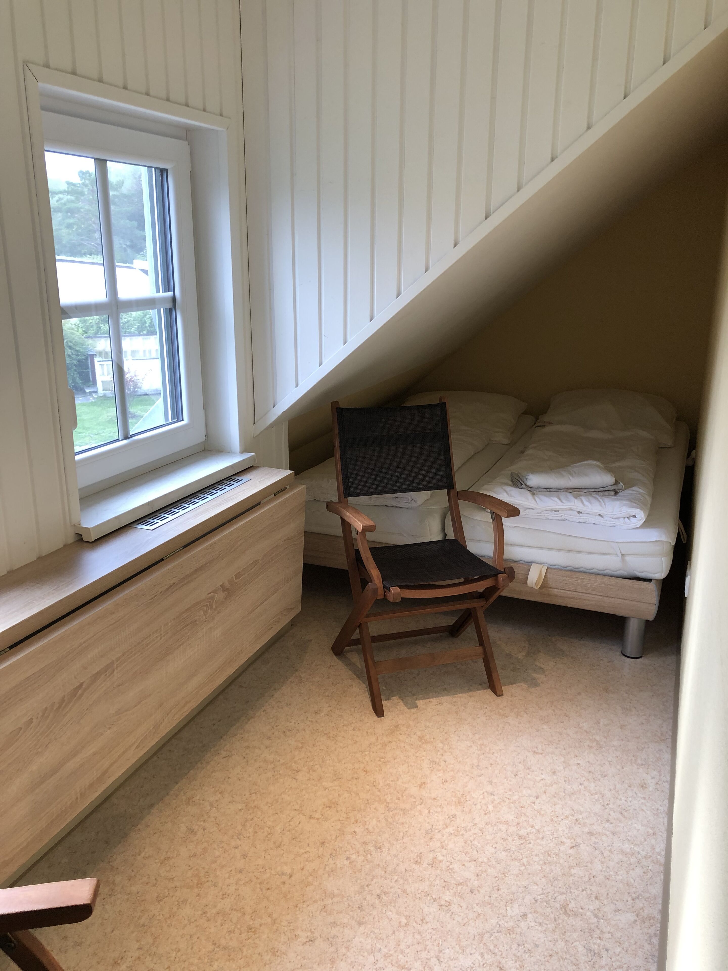Ett litet sovrum på vinden med ett fönster, ett skrivbord, en stol och en säng.