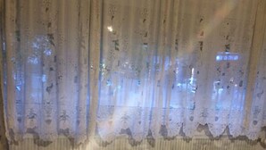 Una habitación con alfombra estampada, una cama con ropa de cama blanca y una ventana con cortinas de encaje.