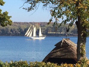 A sailboat on a lake with a thatched-roof structure in the foreground. - Troense B&B by the sea (Svendborg)