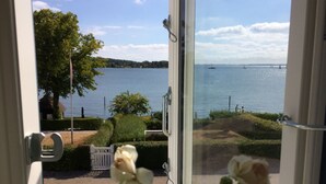 A view through a window of a lake with a boat in the distance, a tree, and a white fence. - Troense B&B by the sea (Svendborg)