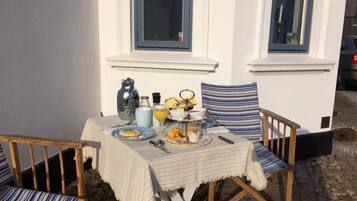 Een buitentafel gedekt met een geruite tafelkleed, twee geruite stoelen, een kan, een theepot, een kopje en een bord met eten.