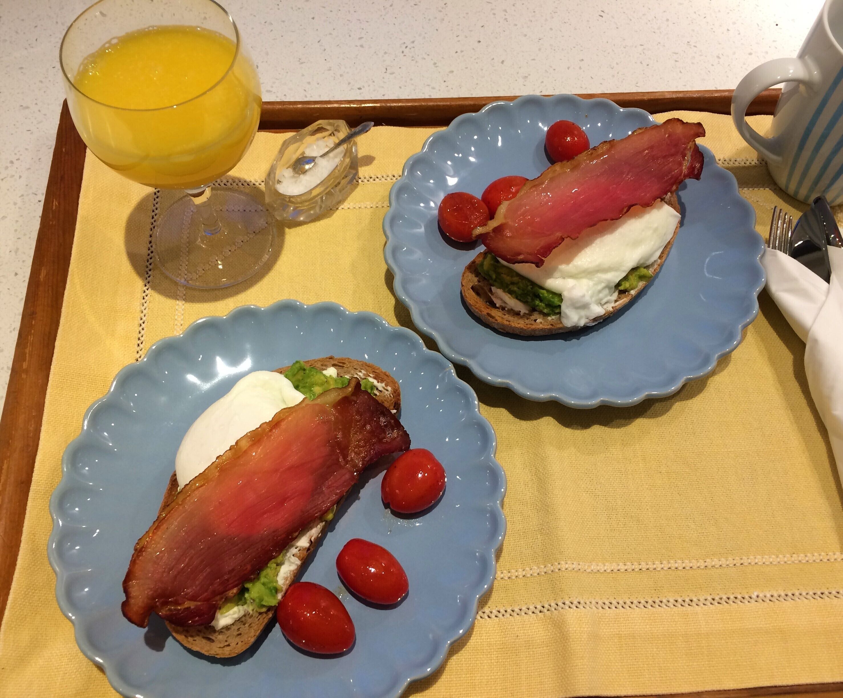 To tallerkener med sandwiches, et glas appelsinjuice og en ske med et hvidt stof på et bord.
