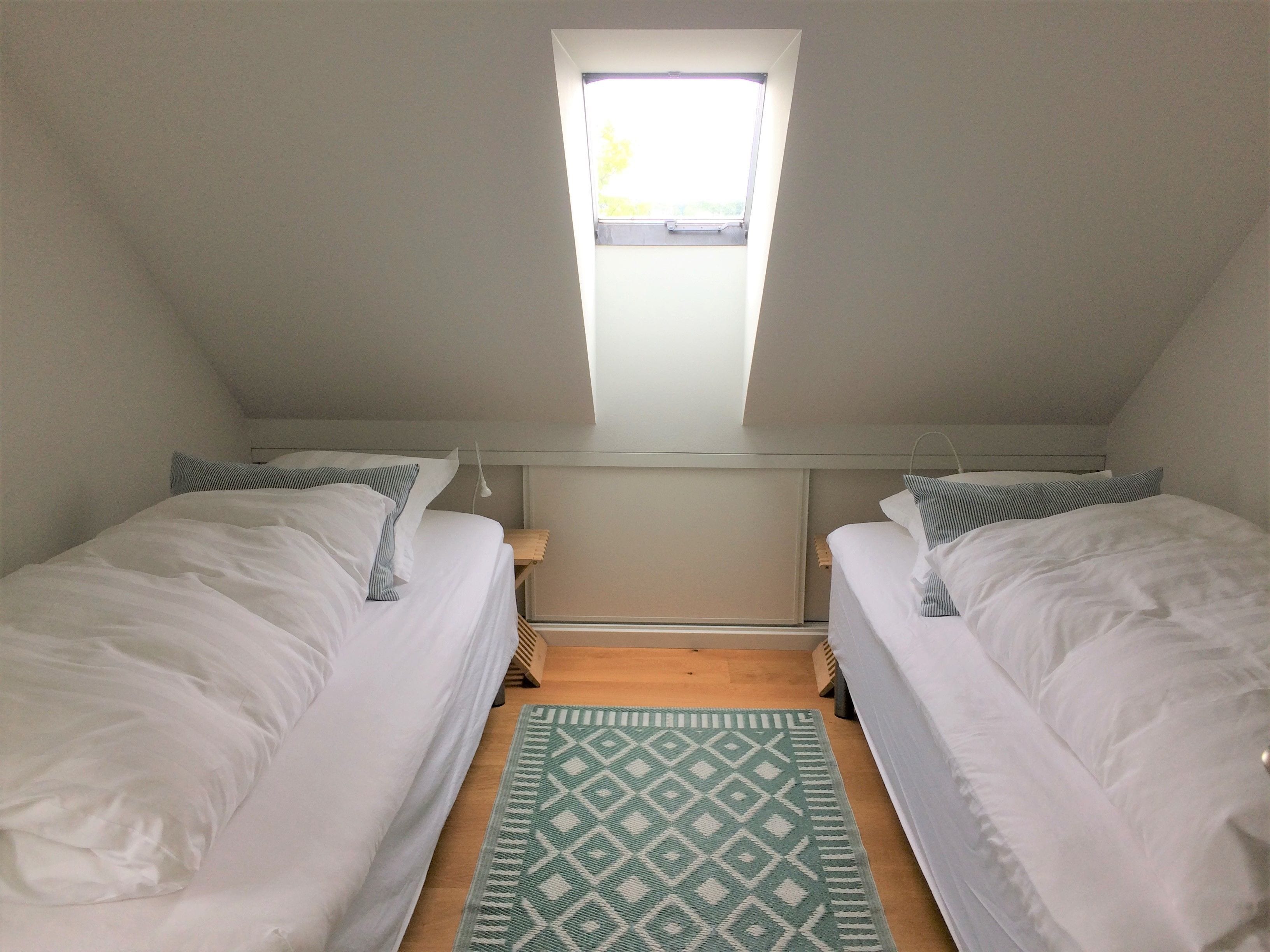 A small, well-lit room with two single beds, a skylight, and a patterned rug.