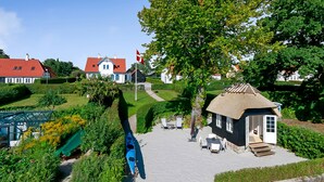 A courtyard with a thatched-roof house, a flag, and a blue kayak. - Troense B&B by the sea (Svendborg)