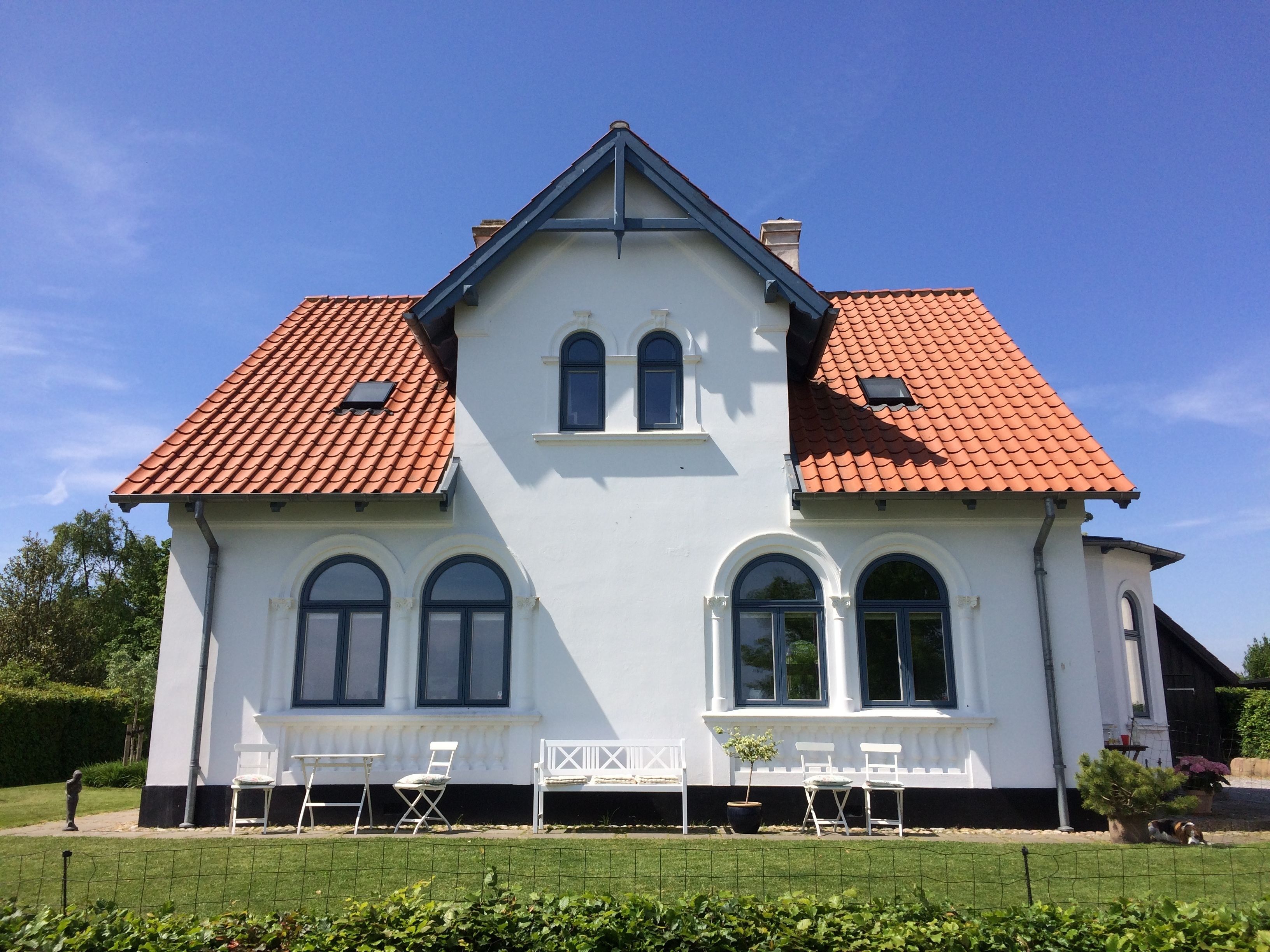 A two-story house with a red-tiled roof, white walls, and a symmetrical facade.
