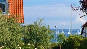 A garden with roses, a building with a red roof, and sailboats on the water. - Troense B&B by the sea (Svendborg)