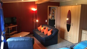 A living room with a sofa, a TV, a lamp, and a wardrobe. - Quiet Holiday home in the middle of the Volcano Eifel (Rheinland-Pfalz)