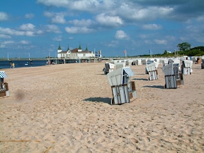 Une plage avec des rangées de chaises de plage numérotées et une jetée sur laquelle se trouve un bâtiment en arrière-plan.