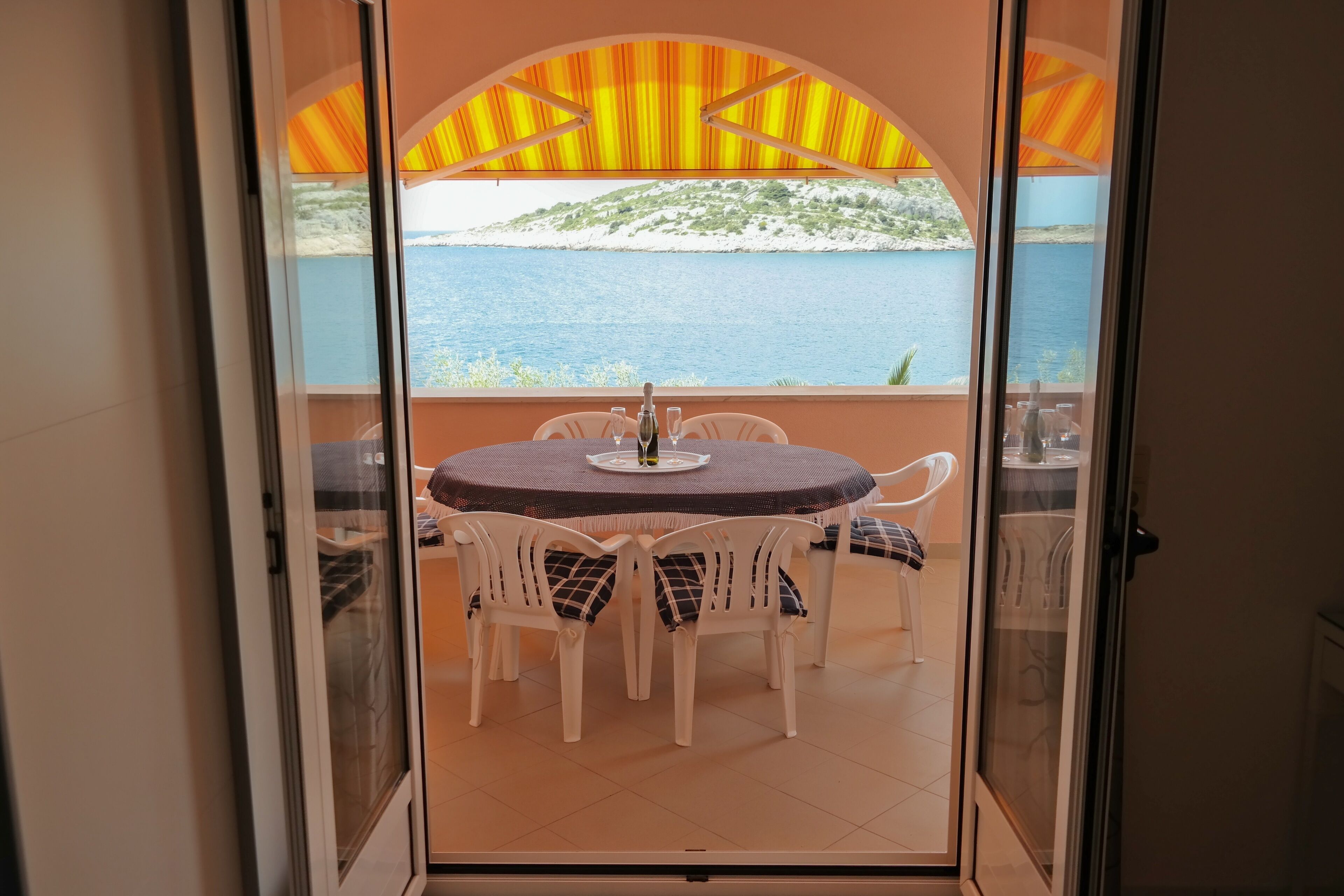 A balcony with a table and chairs, a view of the sea, and a mountainous landscape.