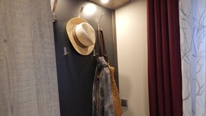 Ein Hotelzimmer mit Holzboden, einer dunklen Tür, einem Hut und einem Schal, der an Haken hängt.