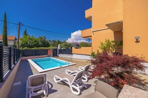 A swimming pool with lounge chairs, a tiled deck, and a building with a yellow exterior. - Suite& Pool (without kitchen) (malinska)