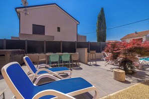 A patio with lounge chairs, a table with chairs, a pool, and a building with a sloped roof. - Suite& Pool (without kitchen) (malinska)