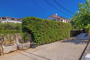 A residential area with a well-maintained hedge, a gravel driveway, and a house with a red-tiled roof. - Suite& Pool (without kitchen) (malinska)