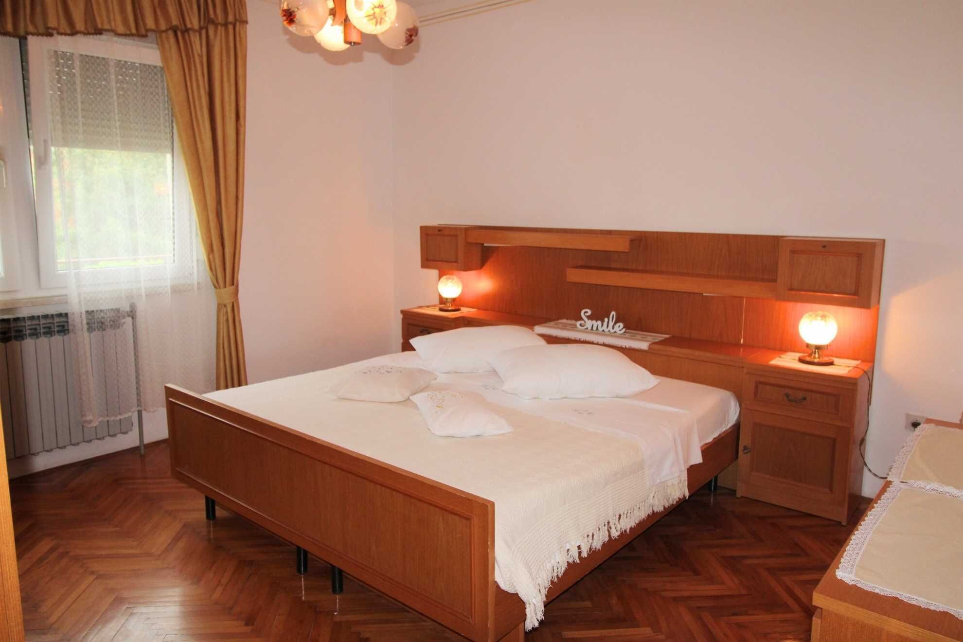 A neatly arranged bedroom with a wooden bed, two bedside tables with lamps, a headboard, and a window with curtains.