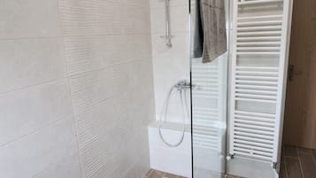 A modern bathroom with a glass shower enclosure, white tiled walls, and a white radiator.