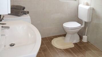 Un baño con lavamanos, inodoro y una ventana sobre el inodoro.