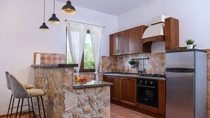 Una cocina compacta con una isla de piedra, armarios de madera, un refrigerador de acero inoxidable y una estufa a gas.