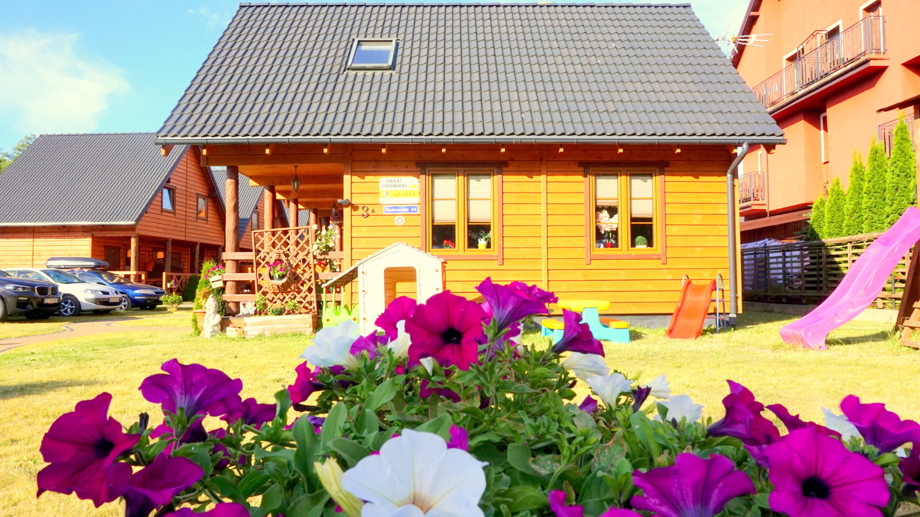 Une cabane en bois avec un toit en pente, une petite véranda et une enseigne indiquant qu’il s’agit d’une maison d’hôtes.