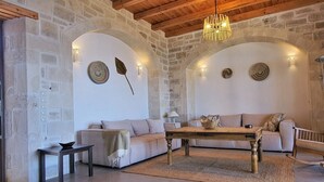 Un saló d'estar acollidor amb parets de pedra, sostre de fusta, un sofà, una taula de centre i decoració mural.