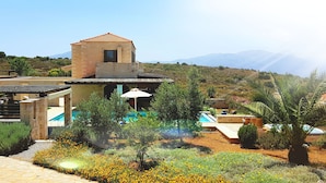 Una vila moderna amb piscina, envoltada de jardins exuberants i un paisatge de muntanyes.