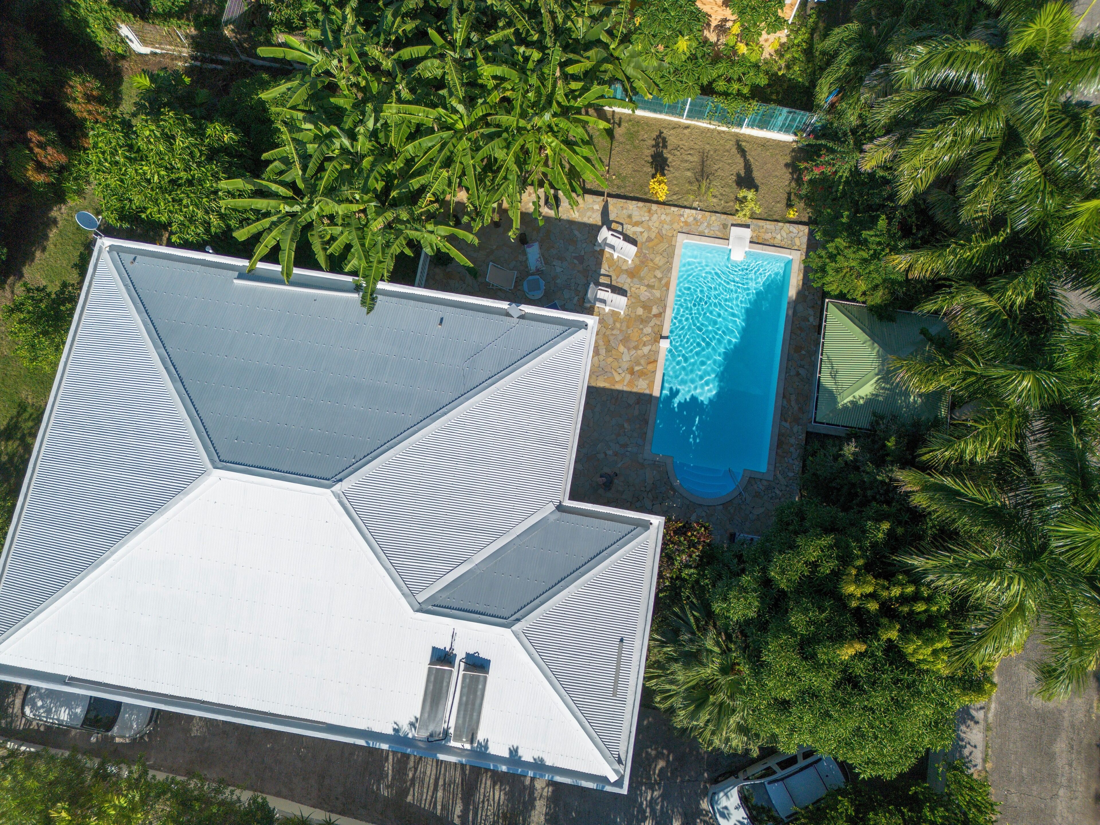 An aerial view of a house with a swimming pool, surrounded by lush greenery and a satellite dish.