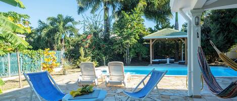 A poolside area with lounge chairs, a hammock, and a covered seating area.