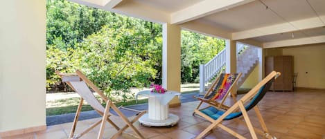 A spacious patio with two wooden swing chairs and a table, overlooking a lush garden and a staircase.