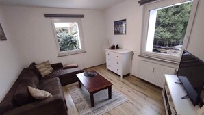 Uma sala de estar com um sofá marrom, uma mesa de centro de madeira, um aparador branco e uma televisão sobre um suporte.