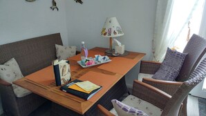 Una habitación con una mesa de madera, sillas de mimbre, un sofá, una lámpara y una ventana con cortinas.