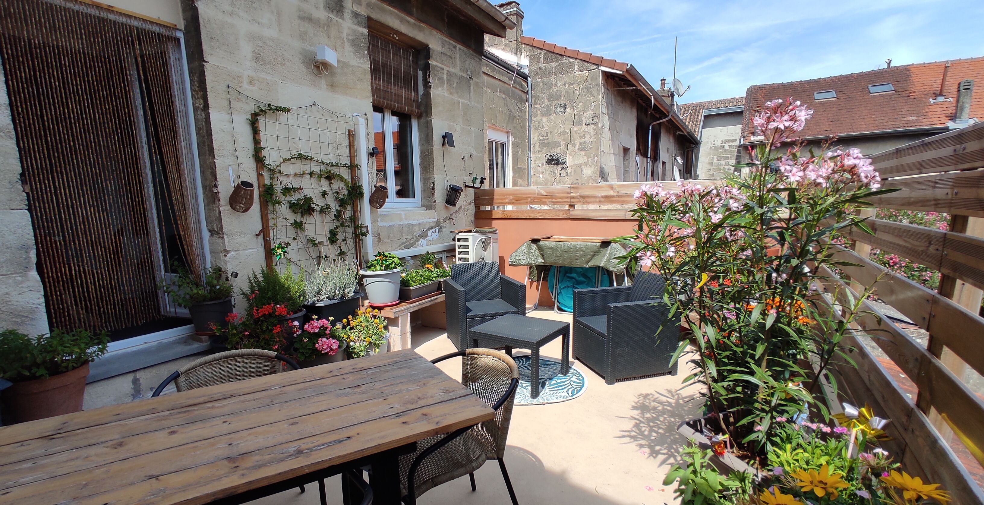 An outdoor patio area with a wooden table and chairs, surrounded by potted plants and flowers.