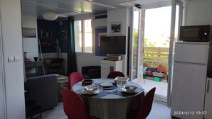 A dining area with a table set for four, a television above the table, and a refrigerator to the right. - Les Bonbonières d'Andréa Gavinies Pellegrin Furnished 2* T2 + private roof top 24 sq.m. (Bordeaux)
