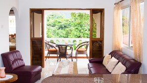 A room with a balcony, a sofa, a table, and wicker chairs.