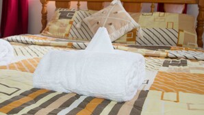 A neatly made bed with a white towel, patterned bedding, and a wooden headboard.