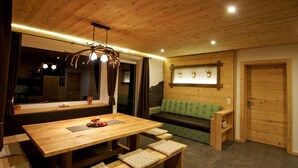 A wooden dining area with a table and benches, a green sofa, and a wall-mounted deer head decoration.