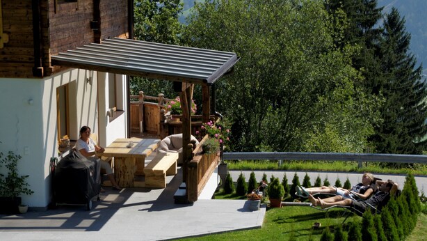 A modern outdoor living area with a wooden deck, a covered seating area, and a landscaped garden with neatly trimmed bushes.