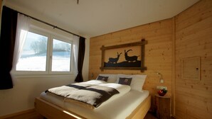A wooden-paneled bedroom with a bed, a window with curtains, and a wall-mounted artwork of deer.