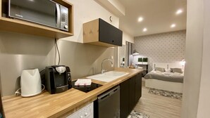 Cocina funcional con microondas, cafetera y lavadora. Se observa también un lavamanos pequeño y un rincón comedor compacto.