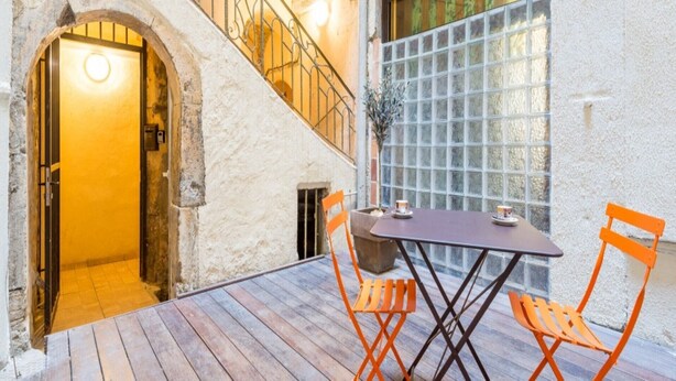 Una terraza de madera con una mesa, sillas, una escalera y un amplio ventanal con vistas.