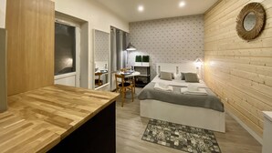 Un dormitorio compacto con cabecera de madera, mesita de noche, cama con almohadas, un pequeño escritorio con silla y un espejo en la pared.