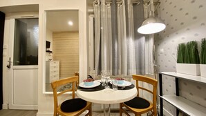 Un comedor con una mesa redonda, dos sillas de madera, una lámpara de techo blanca y una cortina con diseño vertical.