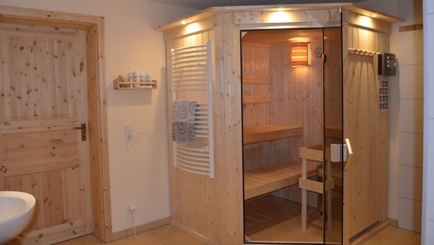 A wooden sauna with a glass door, a towel rack, and a shelf with bottles. - Vacation home at the Bärenstein for 2-8 persons with 140 m² living space, sauna (Struppen)