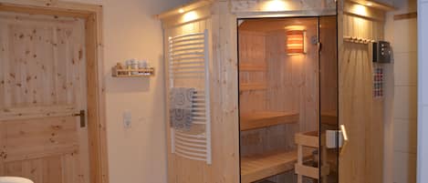 Eine Holzsauna mit Glastür, Handtuchhalter und Ablagefläche mit Flaschen.