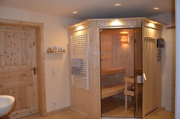 Uma sauna de madeira com porta de vidro, porta-toalhas e prateleira com garrafas.