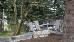 A patio area with a table and chairs, surrounded by trees and a stone wall. - Vacation home at the Bärenstein for 2-8 persons with 140 m² living space, sauna (Struppen)