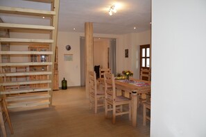 Uma zona de refeições em madeira com mesa e cadeiras, uma escadaria em madeira e uma porta que dá para outro quarto.