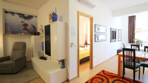 A modern living room with a flat-screen TV, a grey armchair, a dining area with a wooden table and chairs, and a hallway leading to a bedroom. - 2-4 persons, modern furnishings, air-conditioned, washing machine (Porec)
