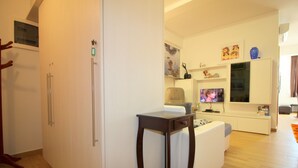 A modern living room with a white sofa, a wooden coffee table, a flat-screen TV, and a white cabinet with shelves. - 2-4 persons, modern furnishings, air-conditioned, washing machine (Porec)