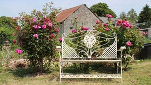 Un banco de metal blanco con diseños intrincados, rodeado de rosales rosados en flor y follaje verde.